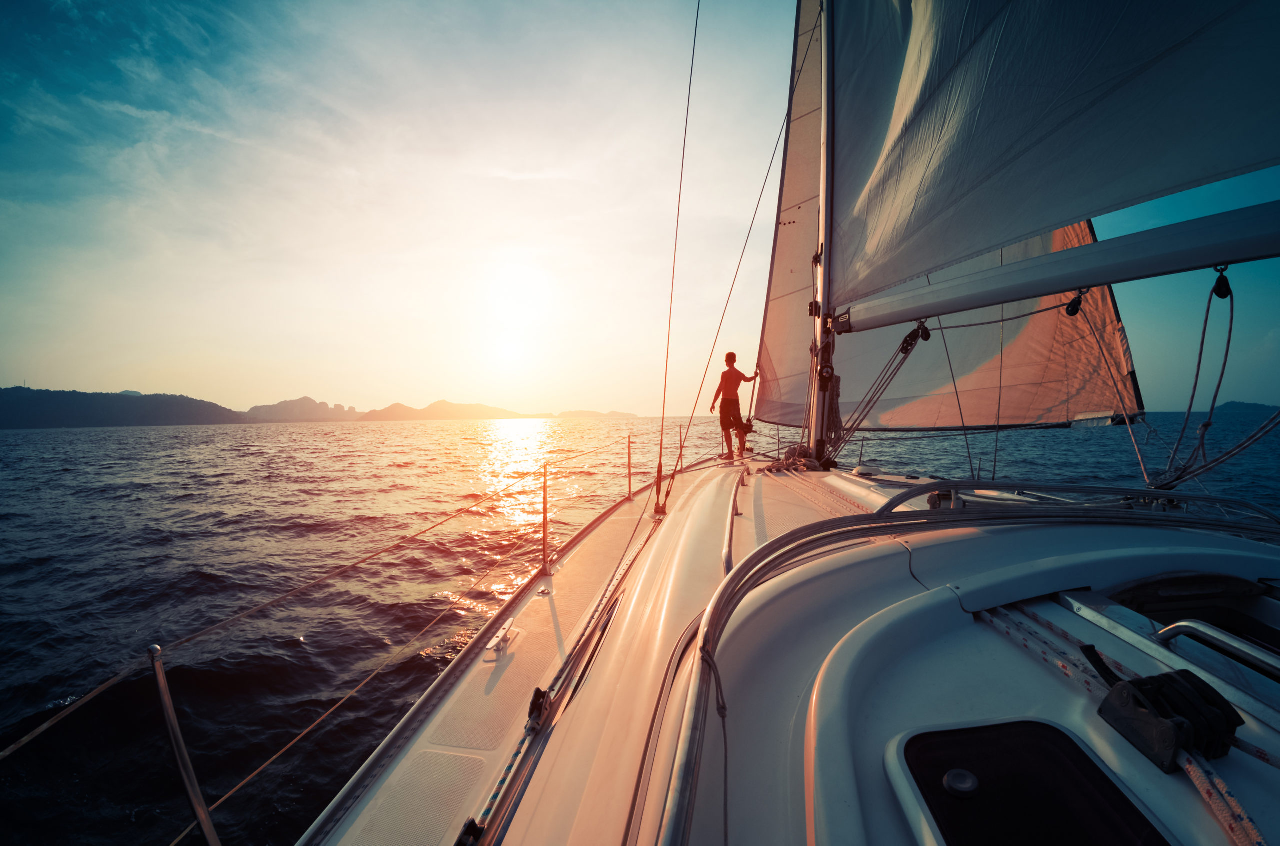 Jeune homme debout sur le yacht dans la mer au coucher du soleil
